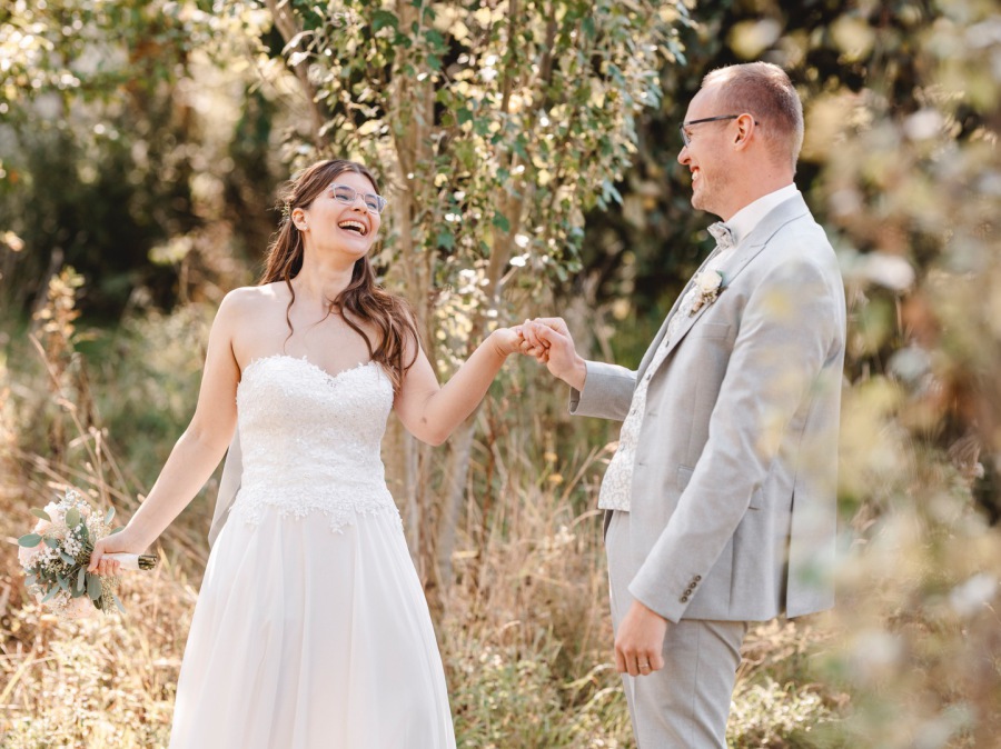 Brautpaar läuft lachend Hand in Hand durch Garten – natürliche Hochzeitsreportage und Paarportrait NRW