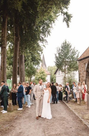 Brautpaar läuft nach der Trauung durch Spalier aus Hochzeitsgästen vor Kirche – natürliche Hochzeitsreportage NRW
