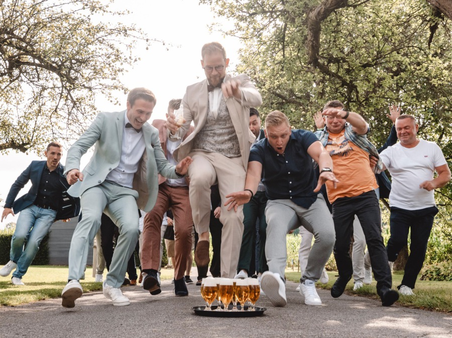 Freunde des Bräutigams springen lachend beim Hochzeitsempfang – lebendige Hochzeitsreportage mit echten Momenten