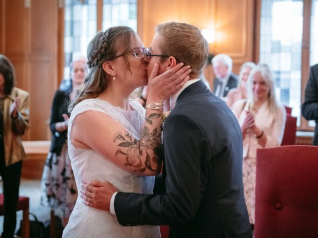 Brautpaar küsst sich nach der standesamtlichen Trauung im Standesamt unter Applaus der Gäste Kuss